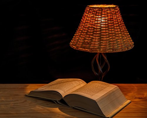 Person reading a book at night with a warm bedside lamp